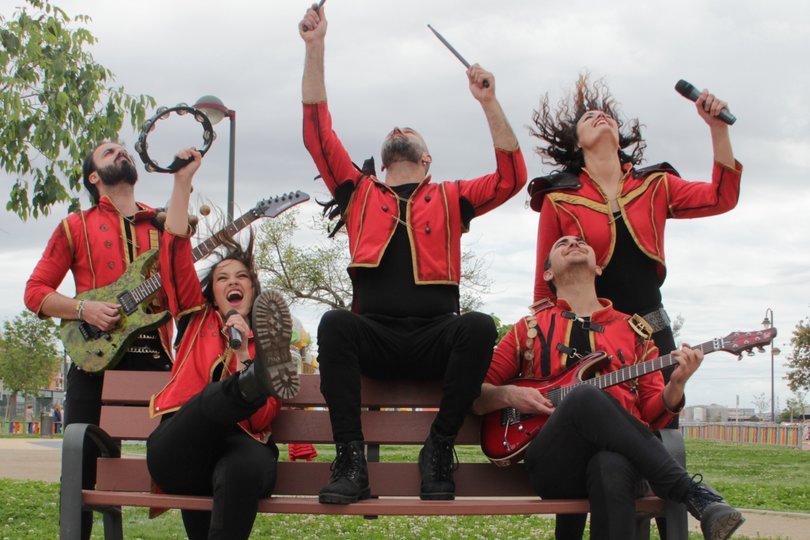 Imagen de 5 personas de una banda posando eufóricos en un banco de un parque