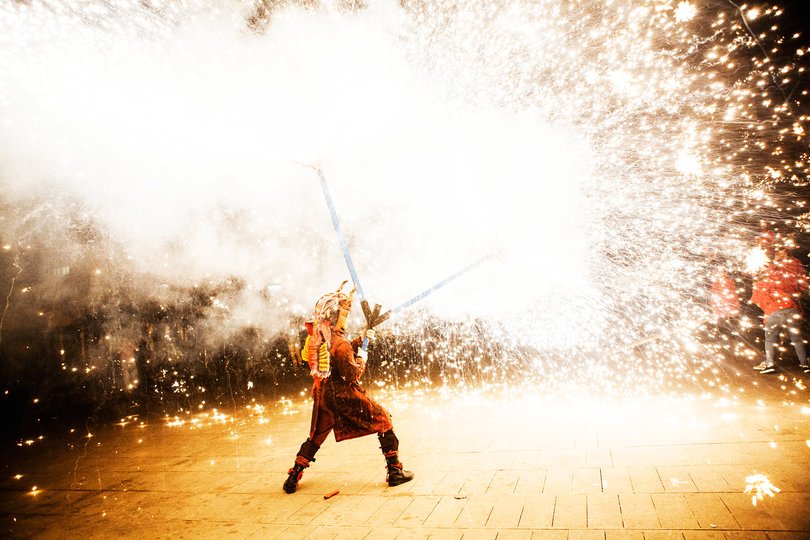Imagen de una persona caracterizada de demonio lanzando un fuego artificial del que salen muchas chispas