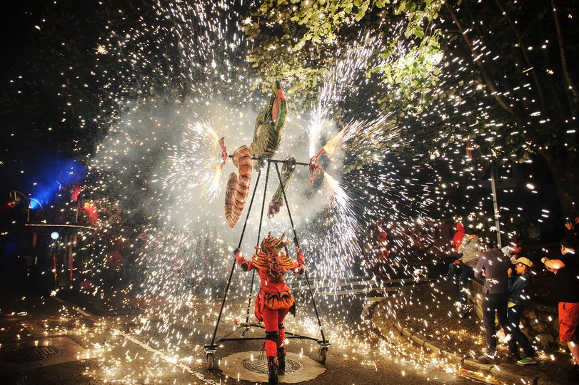 Imagen de una persona caracterizada de demonio sosteniendo una estructura de metal donde hay fuegos artificiales y salen muchas chispas