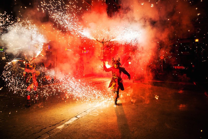 Imagen de una persona caracterizada de demonio lanzando un fuego artificial del que salen muchas chispas rojas