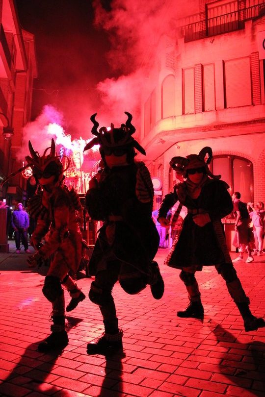 Imagen de personas caracterizadas de demonios luces rojas de bengalas de fondo