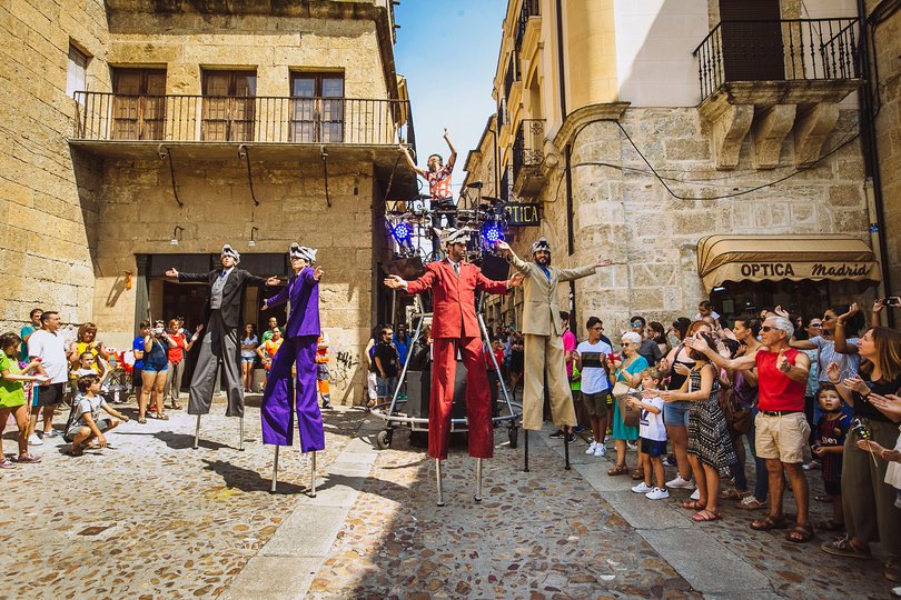 Imagen de 4 personas vestidas con trajes de colores y con máscaras de lobos posando en una plaza rodeados de gente