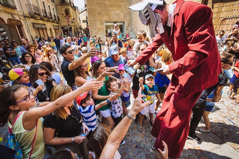 Imagen de una persona vertida con un traje rojo con máscara de lobo repartiendo dinero al el público