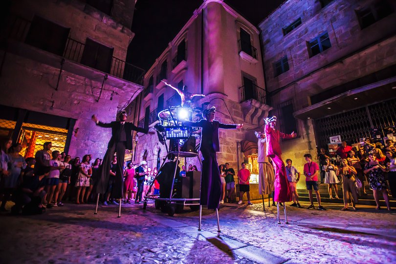 Imagen de 4 personas vestidas con trajes de colores y con máscaras de lobos posando en frente de público de noche e iluminados por varios focos