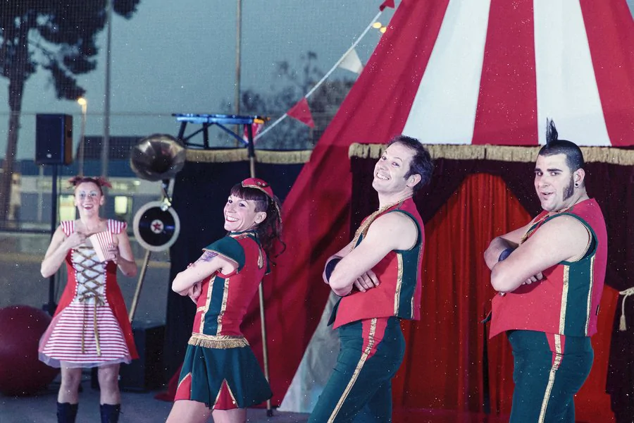 Imagen de 4 personas posando de brazos cruzados con una carpa de circo de fondo