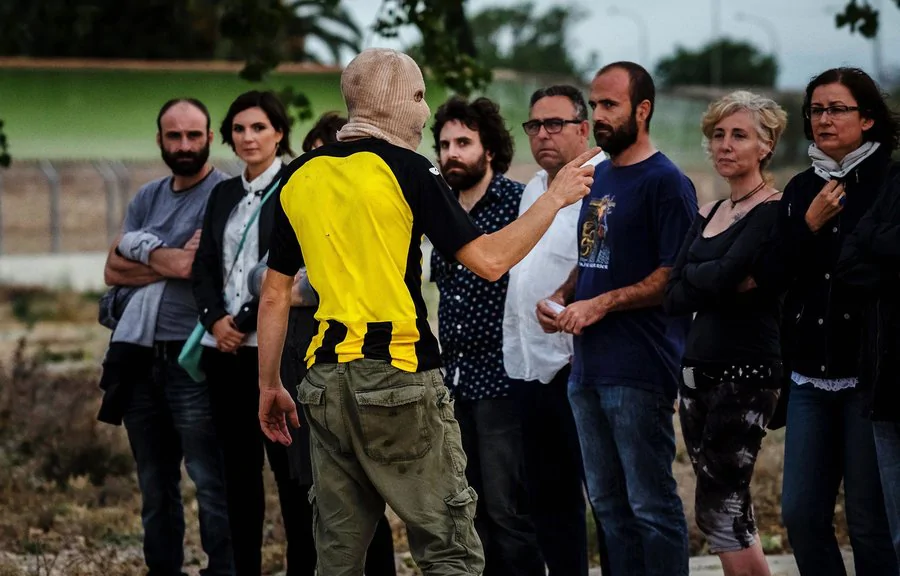 Imagen de una persona con pasamontañas señalando a gente